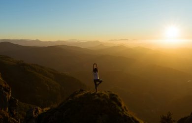 vrouw in yoga pose op een berg bij zonsondergang
